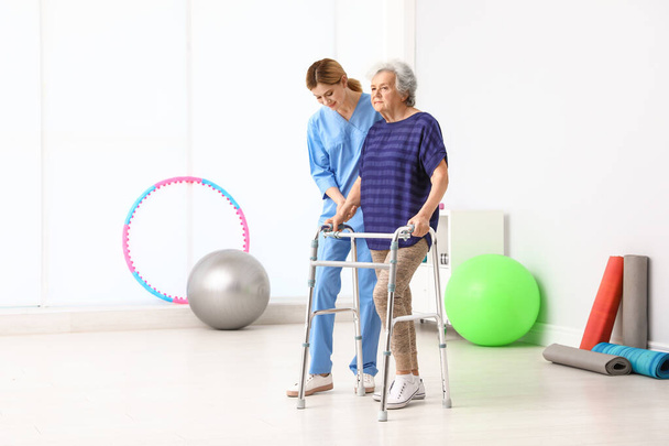 Caretaker helping elderly woman with walking frame indoors - Fotoğraf, Görsel