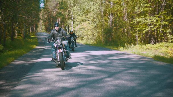 Kaksi moottoripyöräilijää ajaa pölyisellä tiellä metsässä.
 - Valokuva, kuva