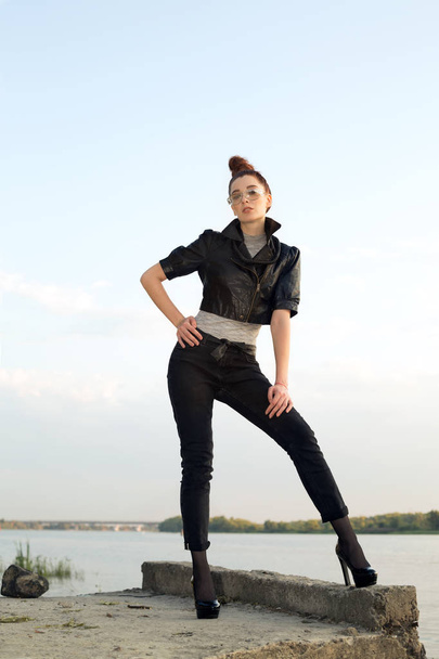 Beautiful woman model in a leather jacket, on the background of the river and the city. - Photo, image