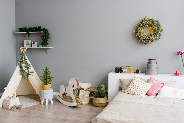 A hálószoba vagy a gyerekszoba belseje karácsonyra vagy szilveszterre díszítve: ágy, paróka, hintaló, karácsonyi koszorú a falon - Fotó, kép