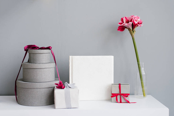 Photobook surrounded by gift boxes, gift and flower in vase on grey wall background - Photo, Image