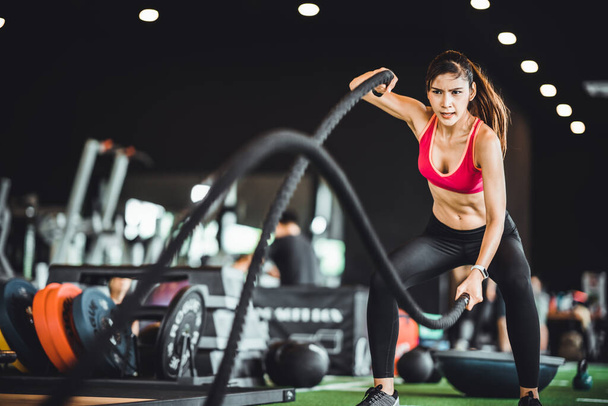 Beautiful Asian woman exercise on battling ropes training equipment in indoor fitness gym. Sport recreational activity, people workout, or healthy lifestyle concept - Foto, Imagem