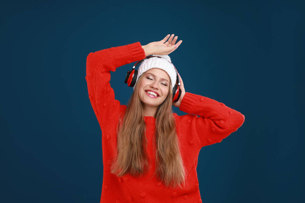 Young woman listening to music with headphones on dark blue background - Valokuva, kuva