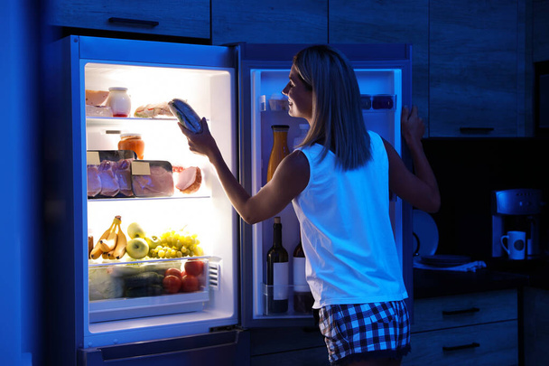 Woman taking sandwich out of refrigerator in kitchen at night - Foto, Imagem