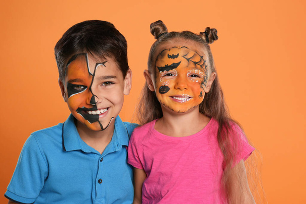Cute little children with face painting on orange background - 写真・画像