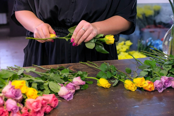 Florist woman prepares flowers to bunch cuts rose thorns in shop, closeup hands. - 写真・画像