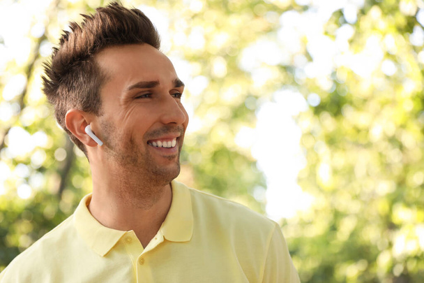 Young man with wireless earphones in park - Zdjęcie, obraz