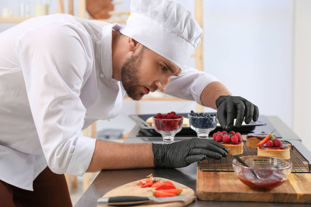 Male pastry chef preparing desserts at table in kitchen - Фото, изображение