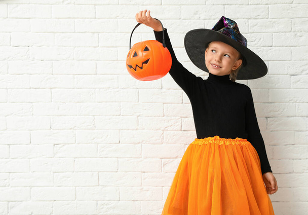 Cute little girl with pumpkin candy bucket wearing Halloween costume near white brick wall. Space for text - Foto, imagen
