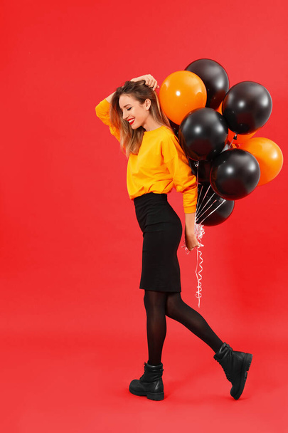 Beautiful woman with balloons on red background. Halloween party - Фото, изображение