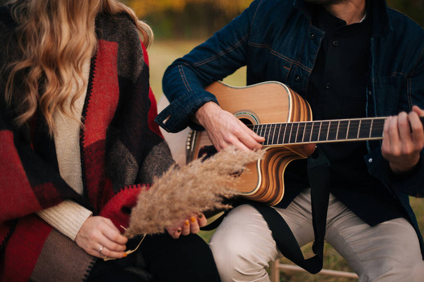 A young couple sitting and playing to the guitar on a field. - Zdjęcie, obraz