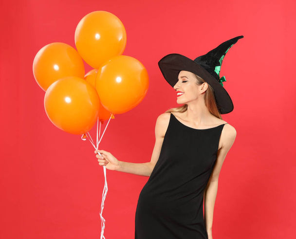 Hermosa mujer con traje de bruja con globos para la fiesta de Halloween sobre fondo rojo
 - Foto, imagen