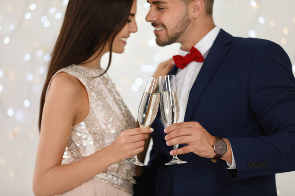 Lovely young couple with glasses of champagne against blurred festive lights, closeup. Christmas celebration - Foto, imagen