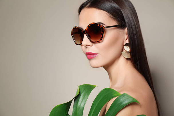 Beautiful woman in stylish sunglasses with tropical leaf on beige background. Space for text - Foto, Bild