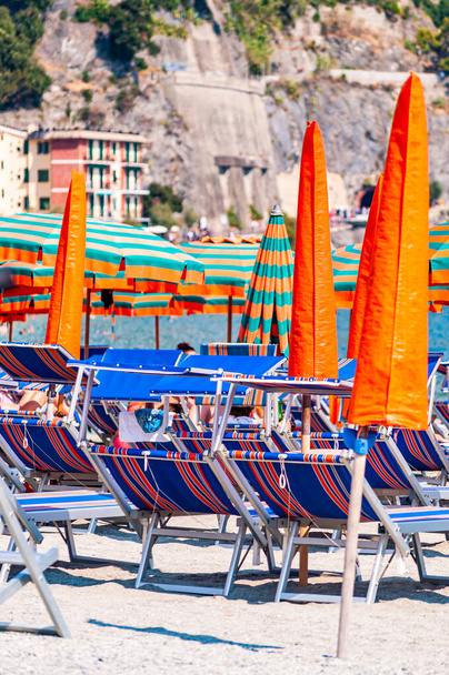 Muchos rayas azul, rojo, tumbonas blancas, sombrillas sombrillas, turistas descansando en la playa de Monterosso Al Mare, Cinque Terre
 - Foto, Imagen
