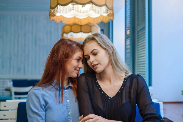 Same-sex relationships. Happy lesbian couple sitting in a cafe. Girls gently hold hands and drink coffee. Embrace of loving women. LGBT. Two best friends in cafe. - Valokuva, kuva