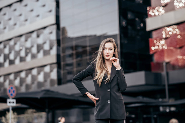 Young and attractive business girl on the background of the city in a beautiful black suit. - Fotografie, Obrázek