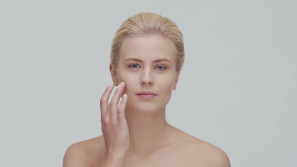 Studio portrait of young, beautiful and natural blond woman applying skin care cream. Face lifting, cosmetics and make-up. - Záběry, video