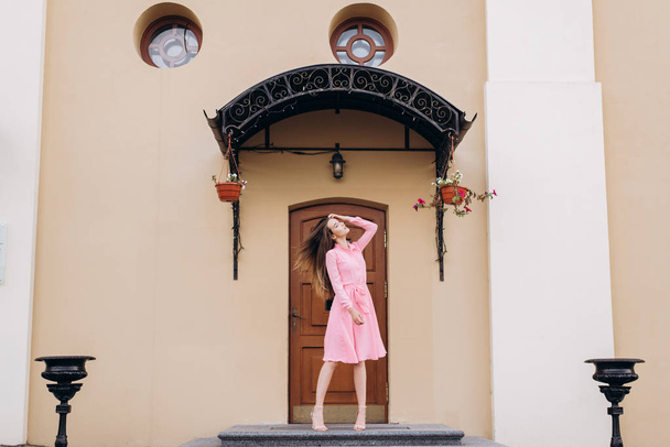 Uma jovem, linda menina em um vestido rosa caminha pela cidade. Foto de perto - para cima e plano geral. Menina sentada em um banco
. - Foto, Imagem