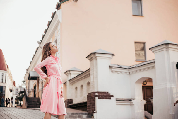 A young, beautiful girl in a pink dress walks through the beautiful streets in the city. Very beautiful portraits of a girl in the city. - Foto, Imagen