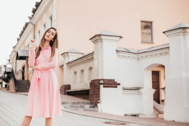 Uma jovem, linda menina em um vestido rosa caminha pelas belas ruas da cidade. Retratos muito bonitos de uma menina na cidade
. - Foto, Imagem