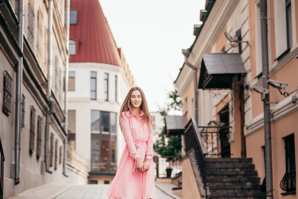 A young, beautiful girl in a pink dress walks through the beautiful streets in the city. Very beautiful portraits of a girl in the city. - Foto, imagen