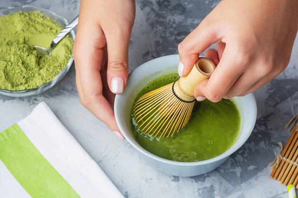 Girl stirs matcha green tea a bamboo whisk. The process of making tea close-up - Zdjęcie, obraz