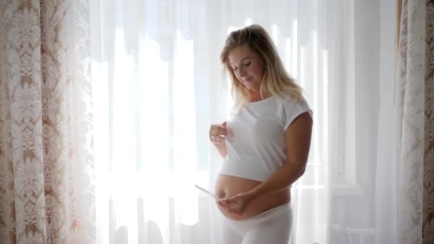 Fröhliches Weibchen berührt dicken Bauch und zeigt zukünftiges Baby im Ultraschall - Filmmaterial, Video