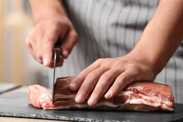 Man cutting fresh raw meat on table in kitchen, closeup - Foto, Imagem