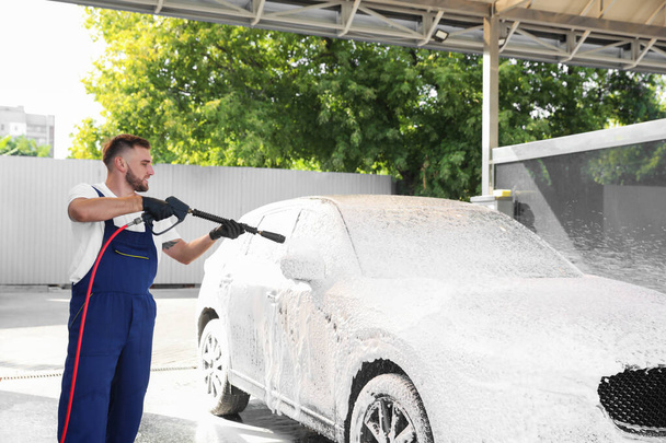 Young worker cleaning automobile with high pressure water jet at car wash - Фото, зображення