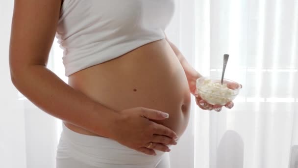 close-up plate with curd in the hand of a pregnant woman near a big naked tummy - 映像、動画