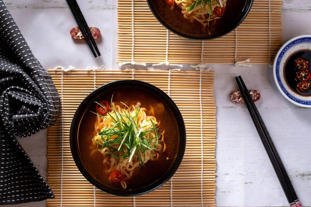 Tésztaleves fekete leves tálakban, bambusz szőnyegen, evőpálcikával és szalvétával az oldalán - Fotó, kép