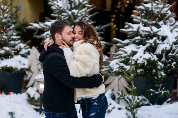Happy couple in warm clothes hugging each other on the background of christmas tree with lights. Winter holidays, Christmas and New Year concept. - Foto, imagen