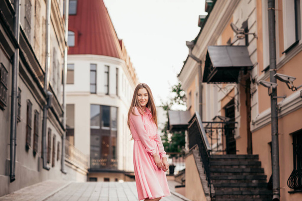 A young, beautiful girl in a pink dress walks through the beautiful streets in the city. Very beautiful portraits of a girl in the city. - Zdjęcie, obraz