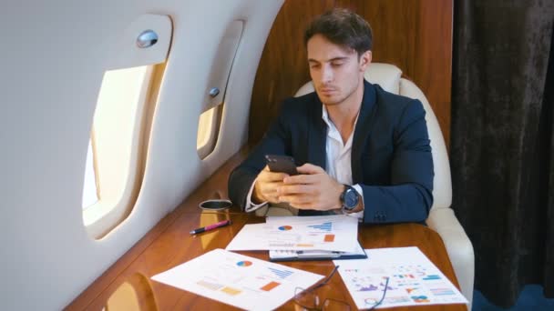 Young handsome chief banker director businessman working using smartphone durung flying in airplane. Successful business man traveling on his private jet plane. - Video