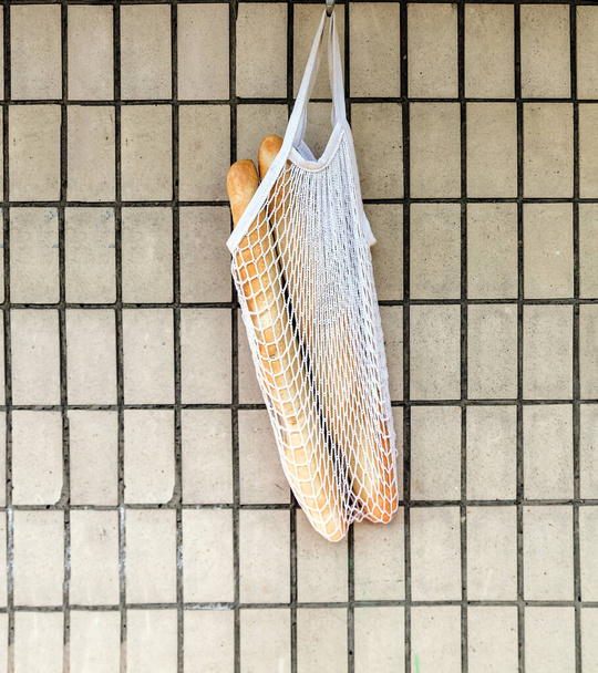 Fresh rosy baguettes in a string bag hanging on a retro brick wall background. Top view, copy space - 写真・画像