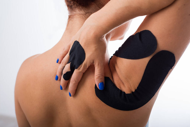 Female shoulder with kineziotape on a white background. Alternative medicine for sports injuries of joints and ligaments. Young sportswoman with a black Medical taping on a sore shoulder and finger. - Foto, afbeelding