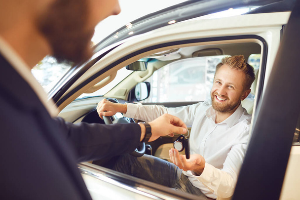 Auto dealer shows a new car to a man - Foto, afbeelding