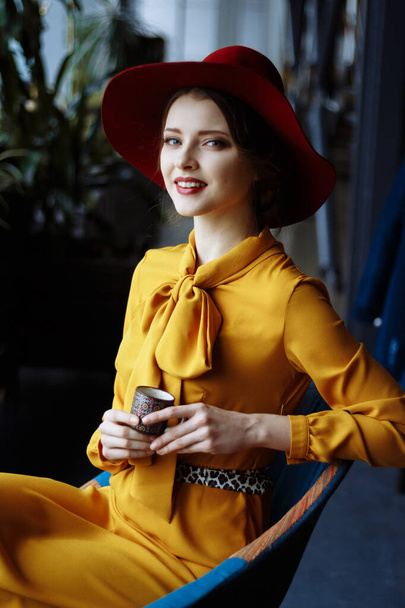 girl in a cafe with a cup of coffee and a hat.portrait of sensual young girl wearing floppy hat and blouse with bow. Beautiful brunette woman in cafe holding cup of coffee - Foto, Imagem