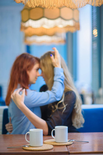Σχέσεις ίδιου φύλου. Ευτυχισμένο ζευγάρι λεσβιών που κάθονται σε μια καφετέρια. Τα κορίτσια κρατούν απαλά τα χέρια και πίνουν καφέ. Αγκάλιασμα των αγαπησιων γυναικών. Λοατ. Δύο καλύτεροι φίλοι στο καφέ. - Φωτογραφία, εικόνα