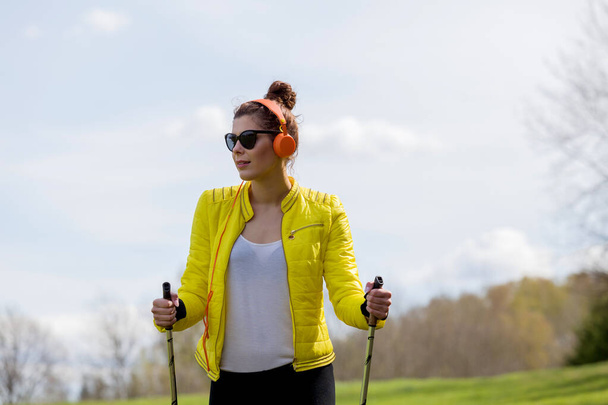 Woman in a yellow jacket and black leggings practicing Nordic wa - Photo, Image
