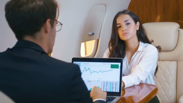 Successful Businesswoman and Businessman fly in a private jet. Woman is looking at the camera. Man works for a laptop. Couple of business people flying a first class plane. - Footage, Video