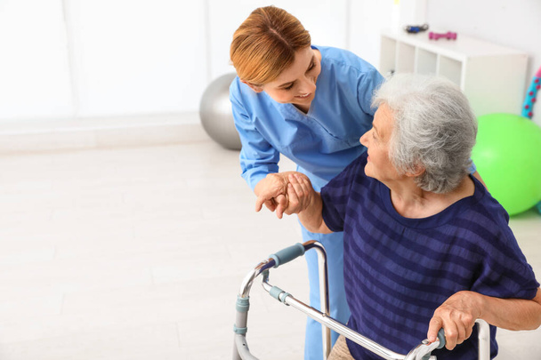 Caretaker helping elderly woman with walking frame indoors - Foto, afbeelding
