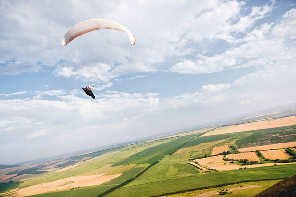 A paraglider flies in the sky in a cocoon suit on a paraglider over the Caucasian countryside with hills and mountains. Paragliding Sport Concept - Photo, image