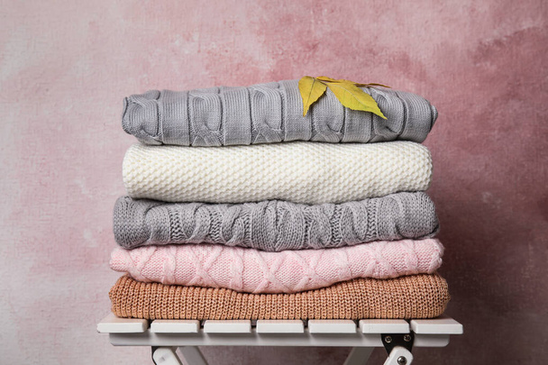 Stack of warm knitted clothes and autumn leaves on white wooden table against pink background - Fotoğraf, Görsel