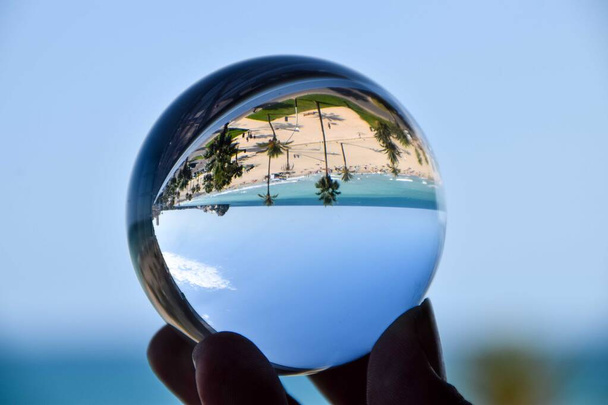Χέρι κρατώντας μια κρυστάλλινη μπάλα με μια παραλία με θέα στη θάλασσα σε αυτό - Φωτογραφία, εικόνα