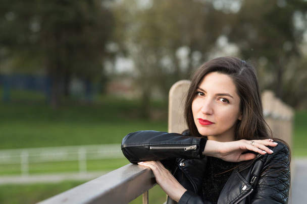 Beautiful brunette in a black jacket and red lips close-up. Closeup of street style fashion Portrait of a beautiful girl in autumn casual outfit Beautiful brunette posing on the street. leather jacket - Photo, Image