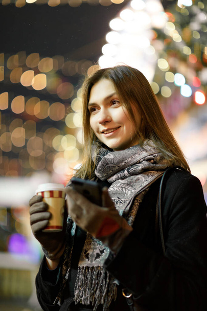 Bild einer glücklichen Frau mit Glas und Handy in der Hand am Abend beim Spaziergang - Foto, Bild