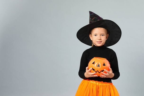 Cute little girl with pumpkin candy bucket wearing Halloween costume on grey background, space for text - Photo, image