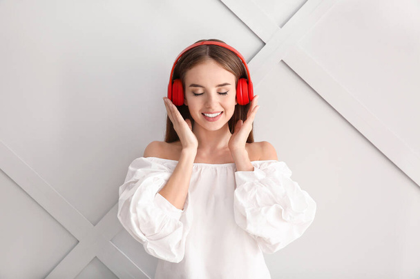 Beautiful young woman listening to music on light background - Foto, Imagen